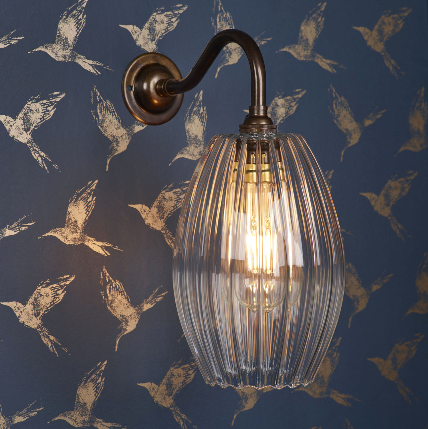 Camber Medium Ribbed Glass Shade Wall Light in an antique brass finish on a navy wall with gold detail